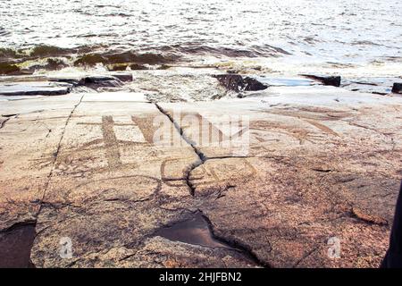 Alte Felszeichnungen am Ufer des Onega-Sees. Geschnitzt auf einer Granitplatte. Kap Besov Nos, Karelien, Russland - 15. August 2021. Stockfoto