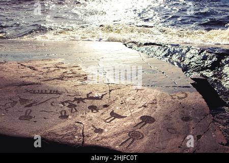 Alte Felszeichnungen am Ufer des Onega-Sees. Geschnitzt auf einer Granitplatte. Kap Besov Nos, Karelien, Russland - 15. August 2021. Stockfoto