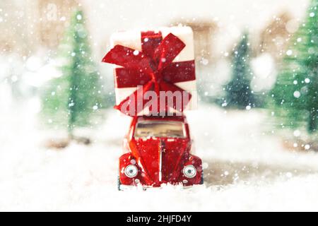 Rotes Retro-Auto mit Geschenkbox in einer Winterlandschaft. Postkarte zum Muttertag oder Valentinstag. Urlaubslieferung. Selektiver Fokus. Stockfoto