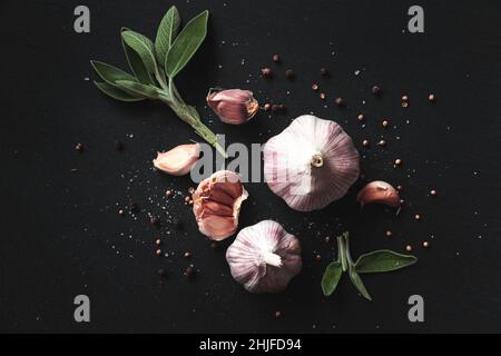 Knoblauchzwiebeln, Gewürze, Kräuter und Knoblauchzehen auf schwarzem Hintergrund. Nahaufnahme, flach liegend, Draufsicht. Lebensmittelhintergrund, selektiver Fokus. Stockfoto