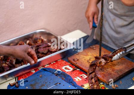 Eine Nahaufnahme eines männlichen Küchenchefs, der ein gekochtes Lamm al Pastor auf einem Holzschneidebret schneidet Stockfoto