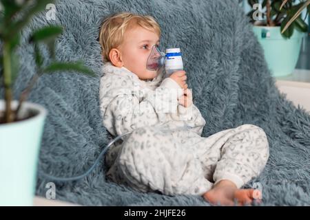 Niedlicher Baby Junge macht Inhalation mit einem Vernebler Ausrüstung. Krankes Kind, das den Inhalator in der Hand hält und zu Hause durch einen Inhalator atmet. Physische Stockfoto