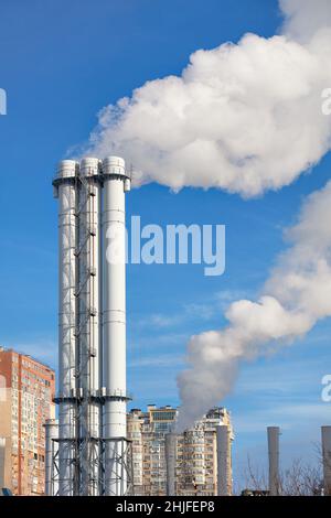 Rauch- und Dampfschwaden steigen aus einer städtischen Thermenanlage in einem Wohnblock in den Himmel. Stockfoto