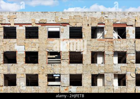 Klaffende leere Fensteröffnungen eines verlassenen Hochhauses gegen einen blau bewölkten Himmel. Stockfoto