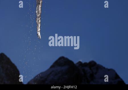 Garmisch Partenkirchen, Deutschland. 29th Januar 2022. Ein Eiszapfen, das von einem Dach hängt, taut im Sonnenschein vor dem Panorama der Alpen auf. Quelle: Karl-Josef Hildenbrand/dpa/Alamy Live News Stockfoto