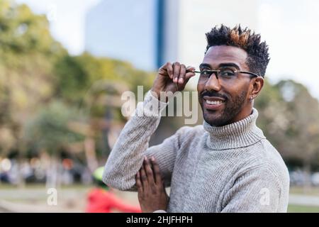 Porträt eines afro-amerikanischen Mannes in einer Weste mit Rollkragen, der seine Brille mit der Hand hält Stockfoto