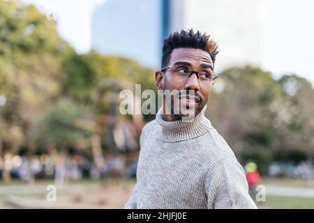 afroamerikanischer Mann, der in einem Park mit Rollkragen zurückblickt Stockfoto