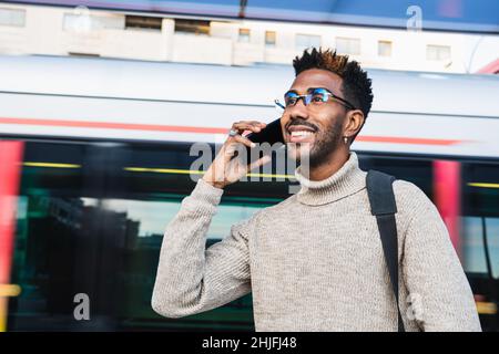 Afroamerikanischer Mann mit Rollkragenweste und Brille, der sein Mobiltelefon benutzte, während er auf den Zug wartete Stockfoto