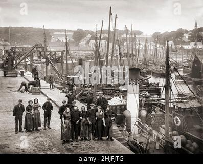 Ein Vintage-Gruppenfoto von Fischern, die im Jahr 1910 neben Dampftrawlern und segelbetriebenen Fischerbooten im Ardglass Harbour, County Down, Nordirland, zu sehen waren. Stockfoto