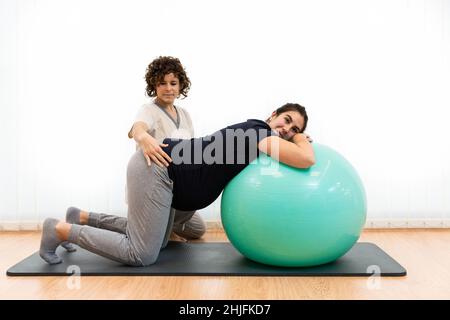 Eine Schwangerin macht Pilates-Übungen mit einem Ball mit Hilfe ihres Physiotherapeuten Stockfoto