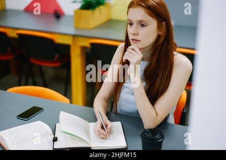 Ernsthafte Frau, die sich Notizen macht, während sie am Tisch sitzt Stockfoto