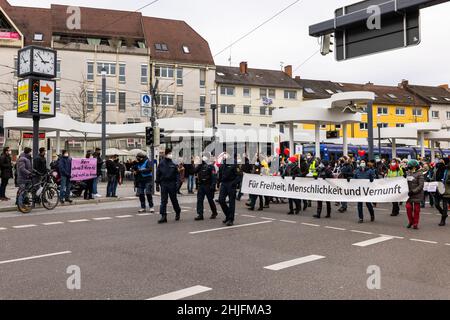 Freiburg, Deutschland. 29. Januar 2022, Baden-Württemberg, Freiburg im Breisgau: Teilnehmer einer Demonstration gegen die Corona-Maßnahmen marschieren mit einem Transparent mit der Aufschrift "für Freiheit, Menschlichkeit und Vernunft" durch Freiburg, während Gegendemonstranten am Straßenrand ein Tuch mit der Aufschrift "Herr schmeiß Hirn ra! Und nicht zu knapp!“. Nach einer ersten Schätzung der Polizei gingen etwa 4.500 Menschen auf die Straße, um gegen die obligatorische Impfung und die Eindämmung der Pandemie zu protestieren. Der Veranstalter hatte rund 7000 Teilnehmer erwartet. Quelle: dpa picture Alliance/Alamy Live New Stockfoto