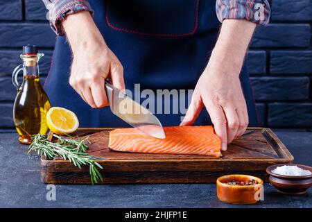 Der Mensch schneidet Lachsfilet. Koch schneidet ein Fischfilet auf einem rustikalen Holzbrett in einer Restaurantküche Stockfoto