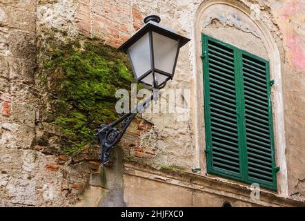 Eine ikonische Laterne auf einer alten Mauer mit grünem Moos in Asciano, Provinz Siena Stockfoto