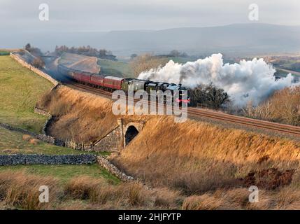 Kirkby Stephen, Cumbria, Großbritannien. 29th Januar 2022. Mit einem starken Seitenwind steigt 'The Winter Cumbrian Mountain Express' auf der Rückreise nach Preston den steilen Anstieg an Birkett Common, nahe Kirkby Stephen, vorbei. Starke Winde verbreiten den Rauch von den Lokomotiven. Das Steam Special brachte die Passagiere auf eine Reise von Preston nach Carlisle über die West Coast Main Line Shap Route und dann von Carlisle zurück nach Preston über die Settle-Carlisle-Linie, wie hier zu sehen ist. Das Special war ein seltener 'doppelköpfiger' Zug, der von zwei Dampflokomotiven 'Leander' und 'Tangmere' gezogen wurde. Quelle: John Bentley/Alamy Live News Stockfoto