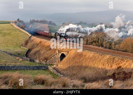 Kirkby Stephen, Cumbria, Großbritannien. 29th Januar 2022. Mit einem starken Seitenwind steigt 'The Winter Cumbrian Mountain Express' auf der Rückreise nach Preston den steilen Anstieg an Birkett Common, nahe Kirkby Stephen, vorbei. Starke Winde verbreiten den Rauch von den Lokomotiven. Das Steam Special brachte die Passagiere auf eine Reise von Preston nach Carlisle über die West Coast Main Line Shap Route und dann von Carlisle zurück nach Preston über die Settle-Carlisle-Linie, wie hier zu sehen ist. Das Special war ein seltener 'doppelköpfiger' Zug, der von zwei Dampflokomotiven 'Leander' und 'Tangmere' gezogen wurde. Quelle: John Bentley/Alamy Live News Stockfoto