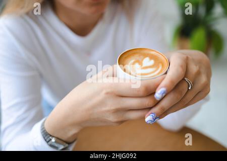 Tasse cremiger Cappuccino-Kaffee in der Hand der Frau. Nahaufnahme von Mädchen halten Tasse mit Aroma Kaffee Stockfoto