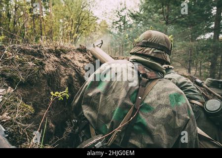 Re-enactors gekleidet, wie Deutsche Wehrmacht Infanterie Soldaten im Zweiten Weltkrieg versteckt Sitzen mit deutschen Hand - Anti-tank Granatwerfer Waffe in einem gehalten Stockfoto