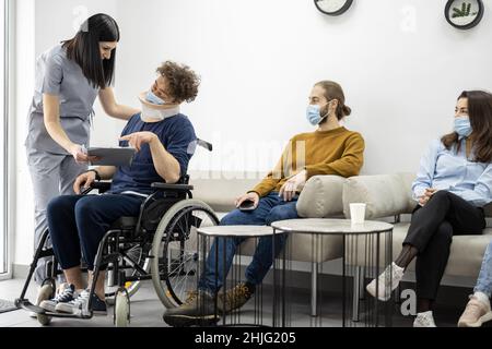 Der Arzt kommuniziert mit dem Rollstuhlfahrer an der Klinikrezeption Stockfoto