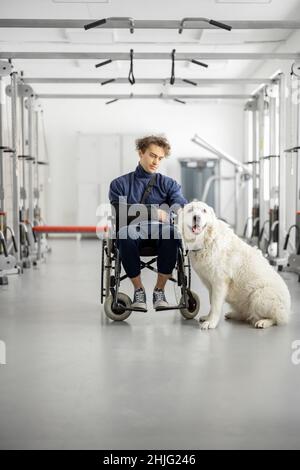 Typ mit Behinderungen im Rollstuhl mit seinem Assistenzhund im Rehabilitationszentrum Stockfoto