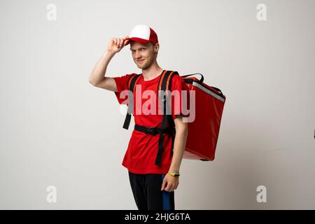 Porträt eines jungen Kuriers in roter Uniform mit einem thermischen Rucksack isoliert auf weißem Hintergrund. Schnelle Lieferung nach Hause. Online-Bestellung. Courier liefert Stockfoto