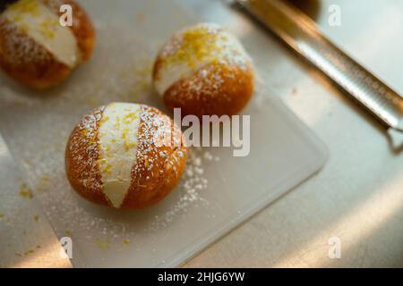 Leckere frische Brötchen mit Creme, verziert mit geriebener Zitronenschale und Puderzucker auf einem Metalltisch Stockfoto
