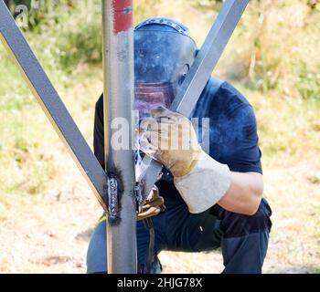 Schweißer-Schweißstrahl mit Schweißmaschine für die Installation von Solarmodulen. Konzept der erneuerbaren und ökologischen Energie. Idee der Umwelt sicher. Mann in schützendem Schweißhelm trägt Arbeitskleidung Stockfoto