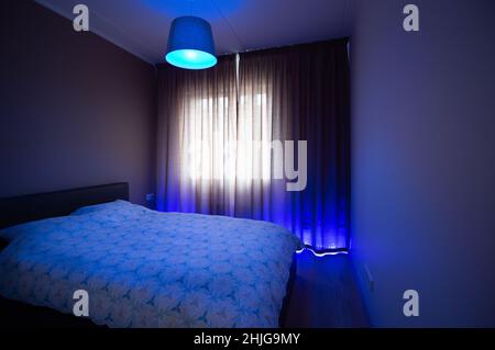 Futuristisch blau beleuchtetes Schlafzimmer mit großem Doppelbett Stockfoto