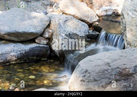 Der langexponige Wasserfall leert über Felsen in einen Pool in einem kleinen Garten Stockfoto