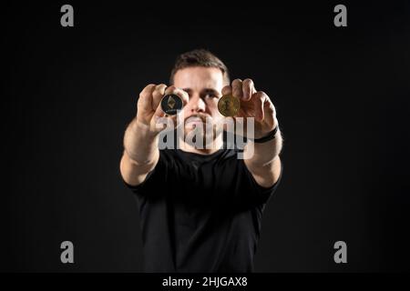 Junger bärtiger Mann mit virtueller Währung ethereum-Münze und Bitcoin auf einem schwarzen Hintergrund-Studio. Kryptowährung. Stockfoto