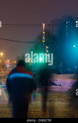 An einem Winterabend überqueren die Menschen an einer grünen Ampel die Straße. Schneit. Stockfoto