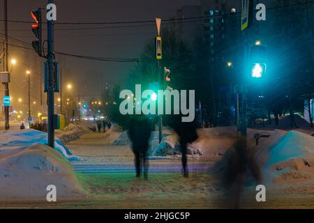 An einem Winterabend überqueren die Menschen an einer grünen Ampel die Straße. Schneit. Stockfoto