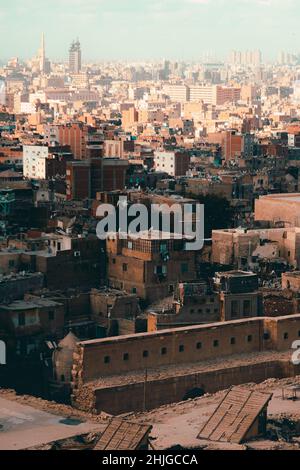 Blick auf zahlreiche Gebäude und Dächer der Stadt Kairo, Multi-Millionen-Hauptstadt mit kleinen Häusern und riesigen Wohnblocks gefüllt. Orangefarbener sandiger moo Stockfoto