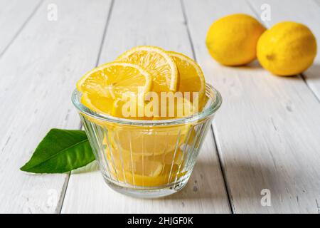 Saftige Zitronenscheiben in einer Glasschüssel auf einem alten weißen Holztisch. Frisch geschnittene gelbe Zitrusfrüchte für Vitamin C, Antioxidans, gesunde Ernährung und Konzepte. Stockfoto