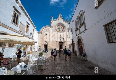 Ostuni, Apulien, Italien. August 2021. Herrlicher Blick auf die Co-Kathedrale von Santa Maria Assunta in Cielo. Menschen auf der Straße und an den Tischen einer Bar.