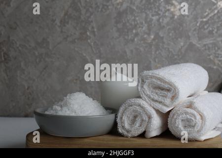 Spa-Behandlungen Entspannung. Körperpflege zu Hause. Weiße Handtuchkerzen Salz für das Bad liegt auf einem Holztablett auf grauem Grund. Stockfoto
