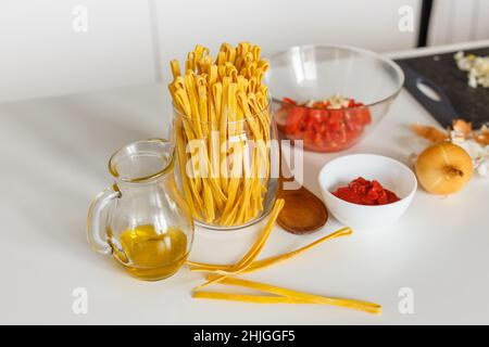 Zutaten aus der Nähe zum Kochen von Bolognese Pasta: Makkaroni, Tomaten, Olivenöl und Zwiebeln. Zubereitung traditioneller italienischer Gerichte aus Nudeln. Konzept der hausgemachten gesunden Lebensmitteln Rezept. Stockfoto