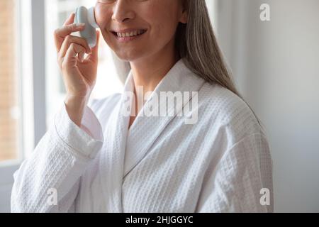 Lächelnde Frau, die Gesichtsmassage mit der Bürste zur Reinigung macht Stockfoto