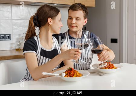 Romantisches Abendessen am Valentinstag zu Hause. Glückliches Paar lächelte, klirrende Gläser und aß Pasta mit Wein in der Küche. Konzept von häuslicher Lebensweise, Liebe, glücklicher Ehe und Zweisamkeit. Stockfoto