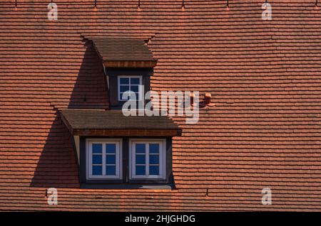 Drei Dachgauben mit Mansardenfenstern in einer mit roten Fliesen überzogenen Dachkonstruktion. Stockfoto