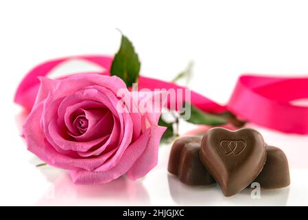 Drei herzförmige Pralinen und rosa Rose auf weißem Hintergrund. Valentinstagskonzept, selektiver Fokus. Stockfoto