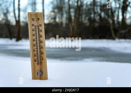 Das Quecksilberthermometer aus Holz, das auf Schnee hängt, weist niedrige Temperaturen auf. Stockfoto