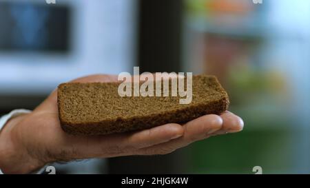 Nahaufnahme der Hand eines Mannes, der ein Stück Borodino-Roggenbrot hält und auf das eine Scheibe Doctor's-Wurst fällt. Köstliches Würstchen-Sandwich Stockfoto