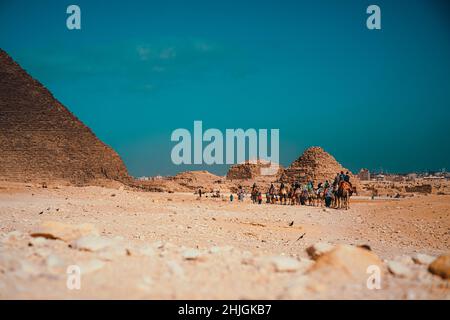 Touristen reiten auf Kamelen in einem Konvoi um die großen Pyramiden von gizeh. Herrliche Aussicht an einem sonnigen Wintertag Stockfoto