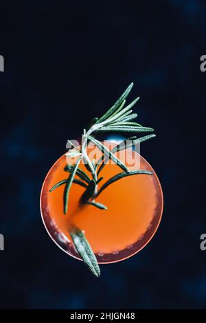 Top-down-Schuss von Orange Karotten Cocktail-Drink mit grünem Rosmarin garniert auf schwarzem Hintergrund Stockfoto