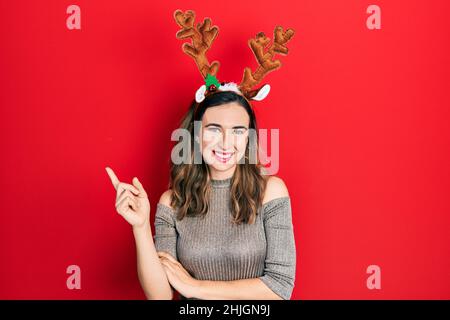 Junge hispanische Mädchen trägt Hirsch weihnachtshut lächelnd glücklich zeigt mit Hand und Finger zur Seite Stockfoto