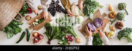 Herbst vegetarische Küche Hintergrund. Mehrere weibliche Hände schneiden und putzen Gemüse auf weißem Tisch mit verschiedenen frischen Gemüse der Saison, Gemüse und Gemüse Stockfoto