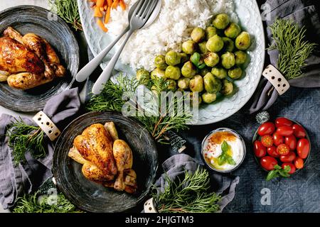 Weihnachts-Esstisch mit gegrilltem Mini-Hähnchen, Reis und Gemüse gebackenen rosenkohl, Baby Karotte in Keramikschüsseln, Weihnachtsdekorationen auf blauem li Stockfoto