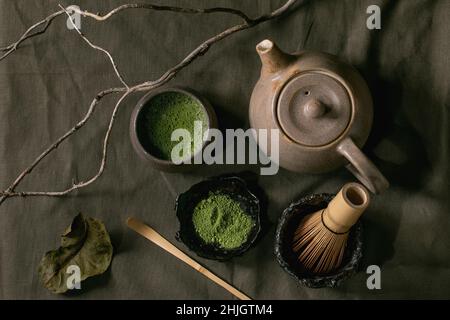 Traditionelle japanische heiße grüne schaumige Tee-Matcha in Keramikbecher, pulverförmige Matcha, Teekannen und Bambusbesen stehen auf dunkler Leinentischdecke. Gesund d Stockfoto
