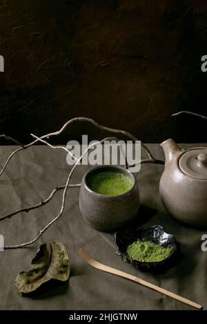 Traditionelle japanische heiße grüne schaumige Tee-Matcha in Keramikbecher, gepuderte Matcha, Teekannen und Bambuslöffel, stehend auf dunkler Leinentischdecke. Gesund Stockfoto